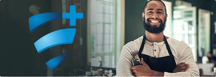 Smiling man with a beard wearing an apron stands with arms crossed in a bright room, next to a large HealthPlus logo on a dark background.
