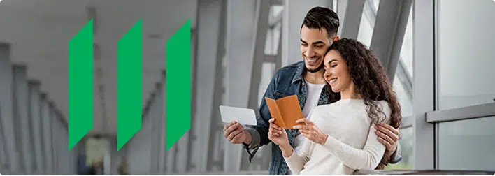 A smiling couple stands in a bright corridor, looking at documents together. The man holds a piece of paper, and the woman holds an open notebook. Manulife logo is on the left side of the image.
