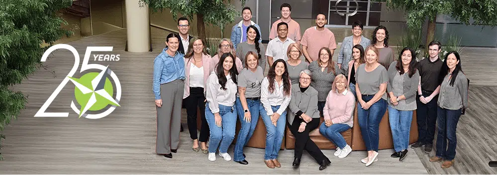 A group of around 20 Selectpath team members pose and smile together indoors near greenery. On the left, a “25 years” anniversary logo is displayed, featuring a green star and circular design.